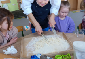 Chłopiec z pomocą nauczycielki przygotowuje ciasto na ciasteczka.