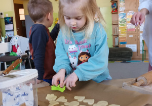 Dziewczynka odkłada na blachę wycięte kształty ciasteczek do upieczenia.