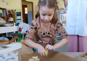 Dziewczynka odkłada na blachę wycięte kształty ciasteczek do upieczenia.