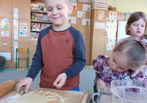 Chłopiec wycina za pomocą foremek kształty ciasteczek z ciasta.