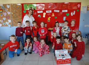 Nauczycielka z dziećmi pozuje do zdjęcia na tle tematycznej dekoracji. Na pierwszym planie znajduje się pudełko na zużyte baterie.