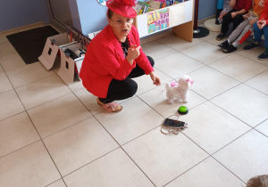 Nauczycielka prowadzi tematyczne zajęcia. W tle na ławeczkach siedzą dzieci.