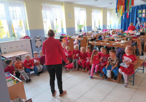 Nauczycielka prowadzi tematyczne zajęcia. W tle na ławeczkach siedzą dzieci.