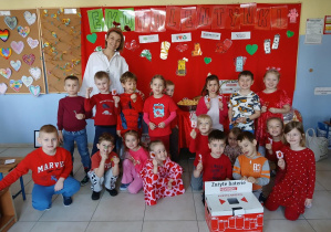 Nauczycielka z dziećmi pozuje do zdjęcia na tle tematycznej dekoracji. Na pierwszym planie znajduje się pudełko na zużyte baterie.