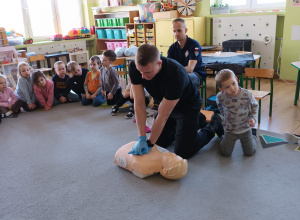 Strażak prezentuje jak wykonać masaż serca na fantomie.