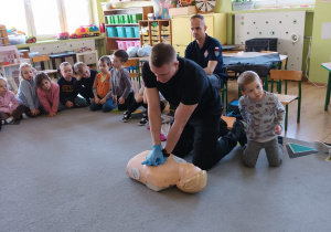 Strażak prezentuje jak prawidłowo wykonać masaż serca.