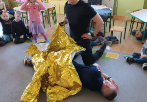 Strażak prezentuje do czego służy koc termiczny.