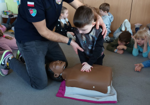 Chłopiec z pomocą strażaka wykonuje masaż serca.