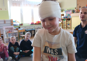 Chłopiec prezentuje opatrunek wykonany przez strażaka.