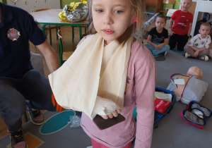 Dziewczynka prezentuje opatrunek wykonany przez strażaka.