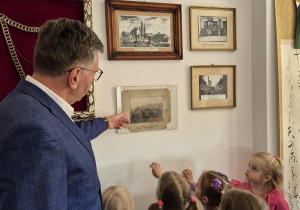 Burmistrz prezentuje dzieciom pamiątkowe obrazy.