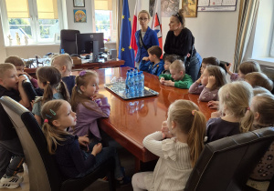 Dzieci siedzą przy stole i słuchają wykładu Burmistrza.
