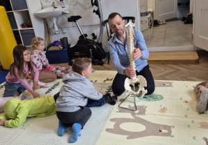 Fizjoterapeuta prezentuje dzieciom model kręgosłupa.