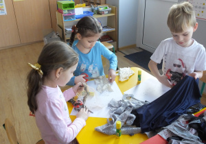 troje dzieci ogląda tkaniny leżące na stole