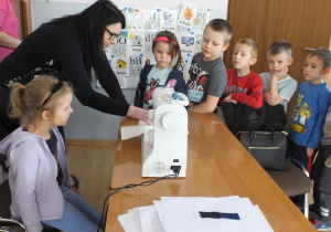 krawcowa prezentuje grupie dzieci, jak szyje się na maszynie