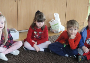 czworo dzieci siedzi na dywanie i słucha