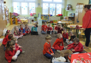 dzieci siedzą na dywanie , słuchają co mówi nauczycielka