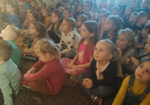 dzieci siedzą na dywanie i oglądają przedstawienie