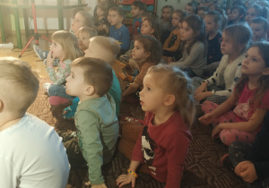 dzieci siedzą na dywanie i oglądają przedstawienie
